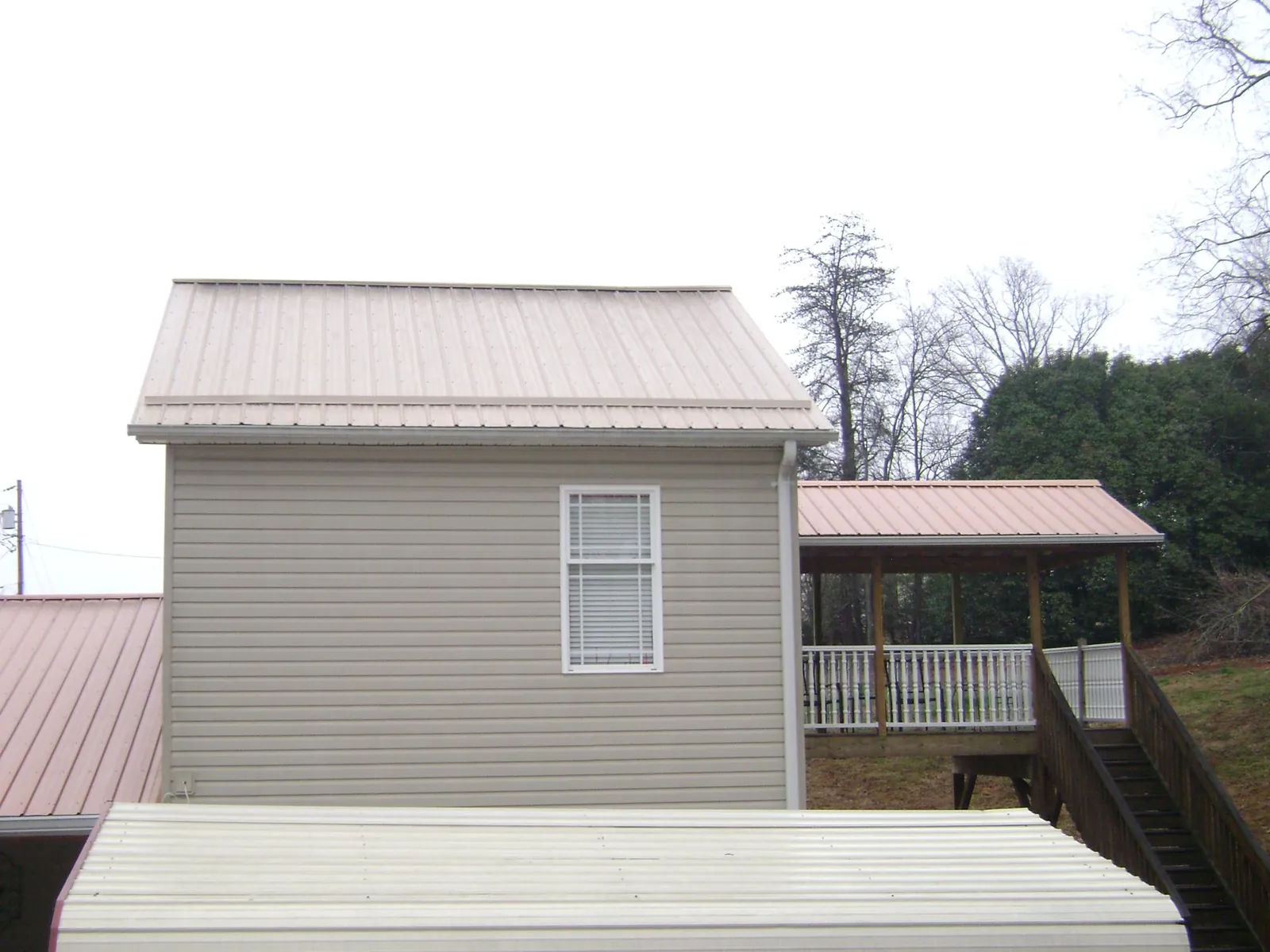Tan metal roofs on a two story addition and attached porch, from a Roof Replacement job in Hudson